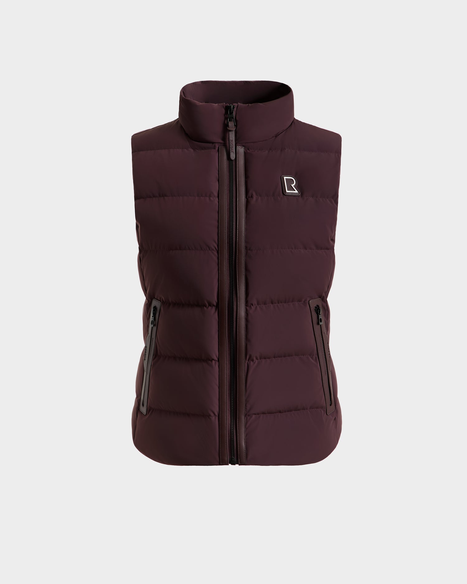 The Rudsak GABRIELA - 8125014 Bordeaux is a maroon women’s down puffer vest with vegan leather trim, a front zipper, two zippered side pockets, and an embroidered R logo on the left chest, shown on a white background.