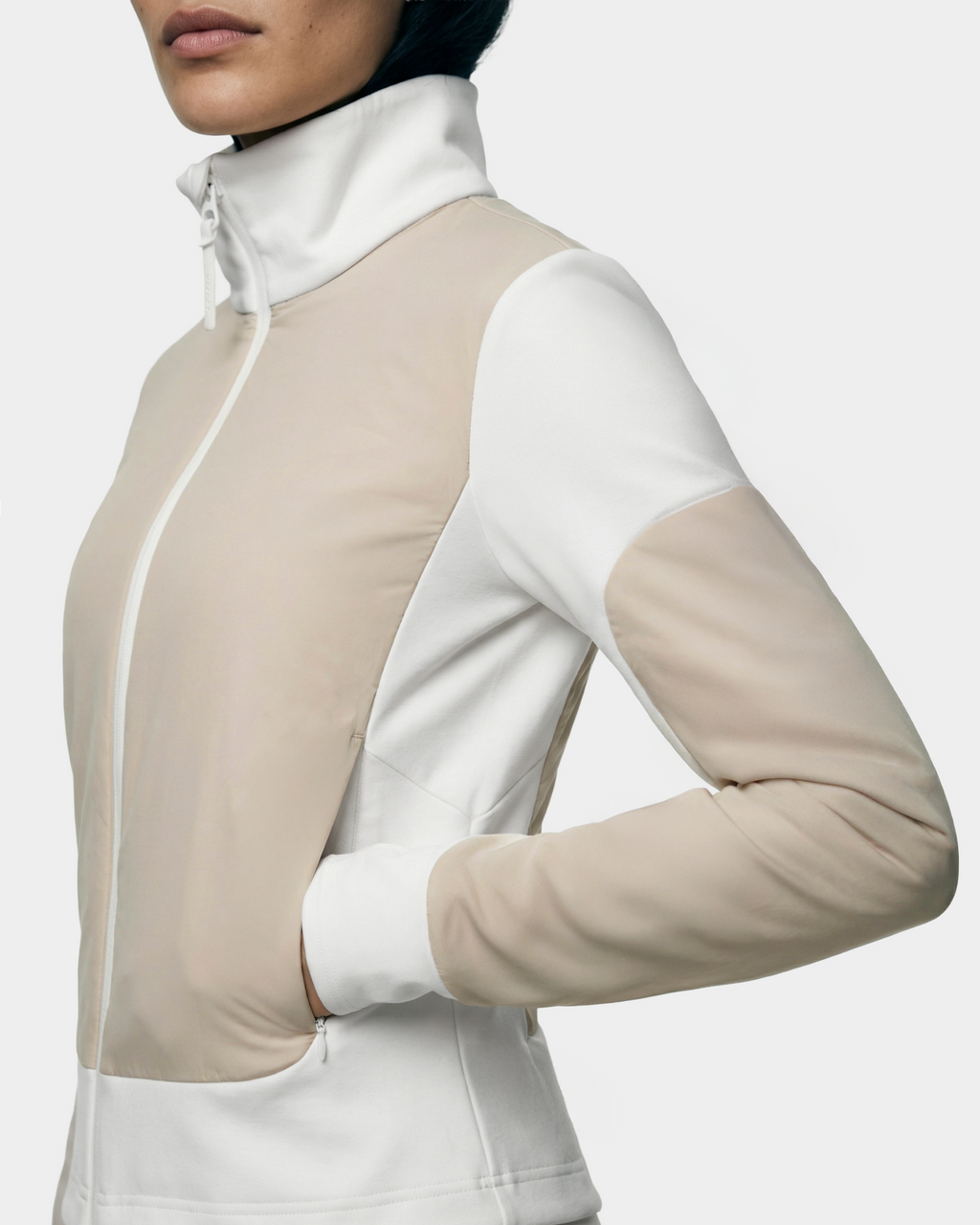 Wearing the Rudsak GRANADA - 8126023 Vanilla zip-up sweater jacket in white and beige, a person stands with one hand in their pocket, highlighting its sporty-chic style and everyday comfort against a plain background.