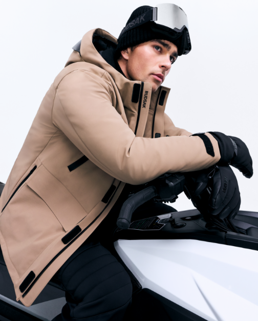 Person wearing a beige winter coat and black gloves sitting on a motorcycle.