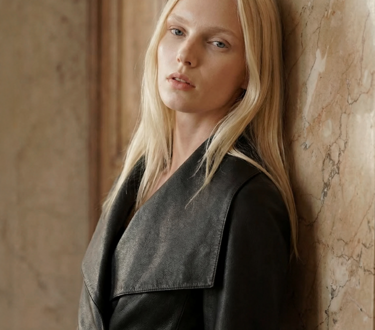 Woman leaning against a textured wall wearing a dark sleeveless top.