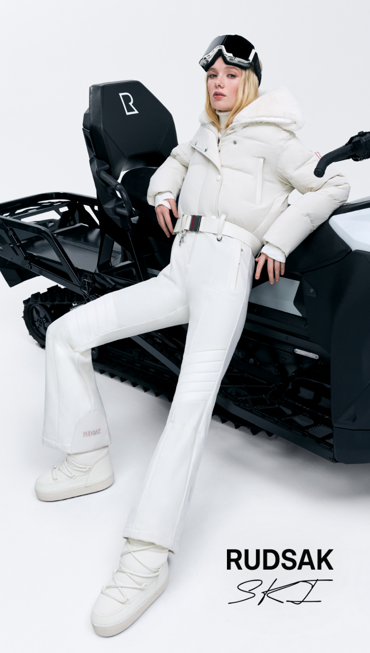 Person in white ski outfit sitting on a black snowmobile with 'RUDSAK SKI' branding.