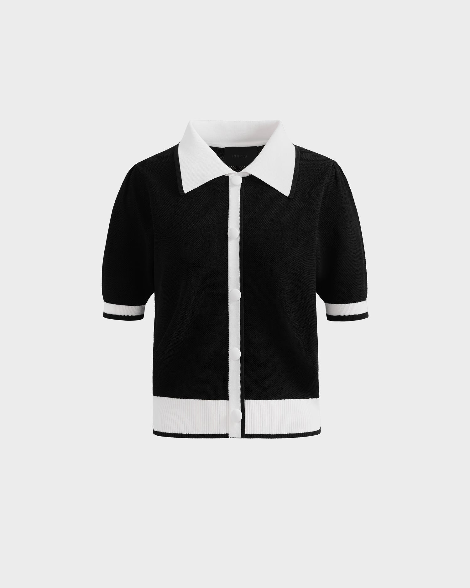 The Rudsak IRIS - 8526012 Black is a black knit short-sleeve sweater featuring white buttons, a contrast collar, and white trim on the cuffs and hem, shown against a plain light background.