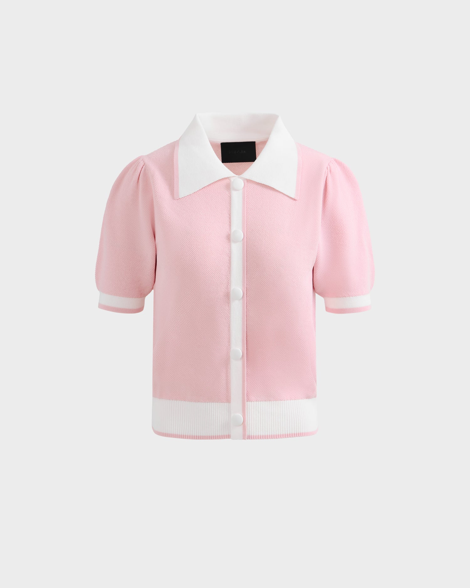 The IRIS - 8526012 Pink by Rudsak is a light pink knit short-sleeve sweater with a contrast collar, white front buttons, and white trim on the sleeves and hem, shown against a plain light gray background.