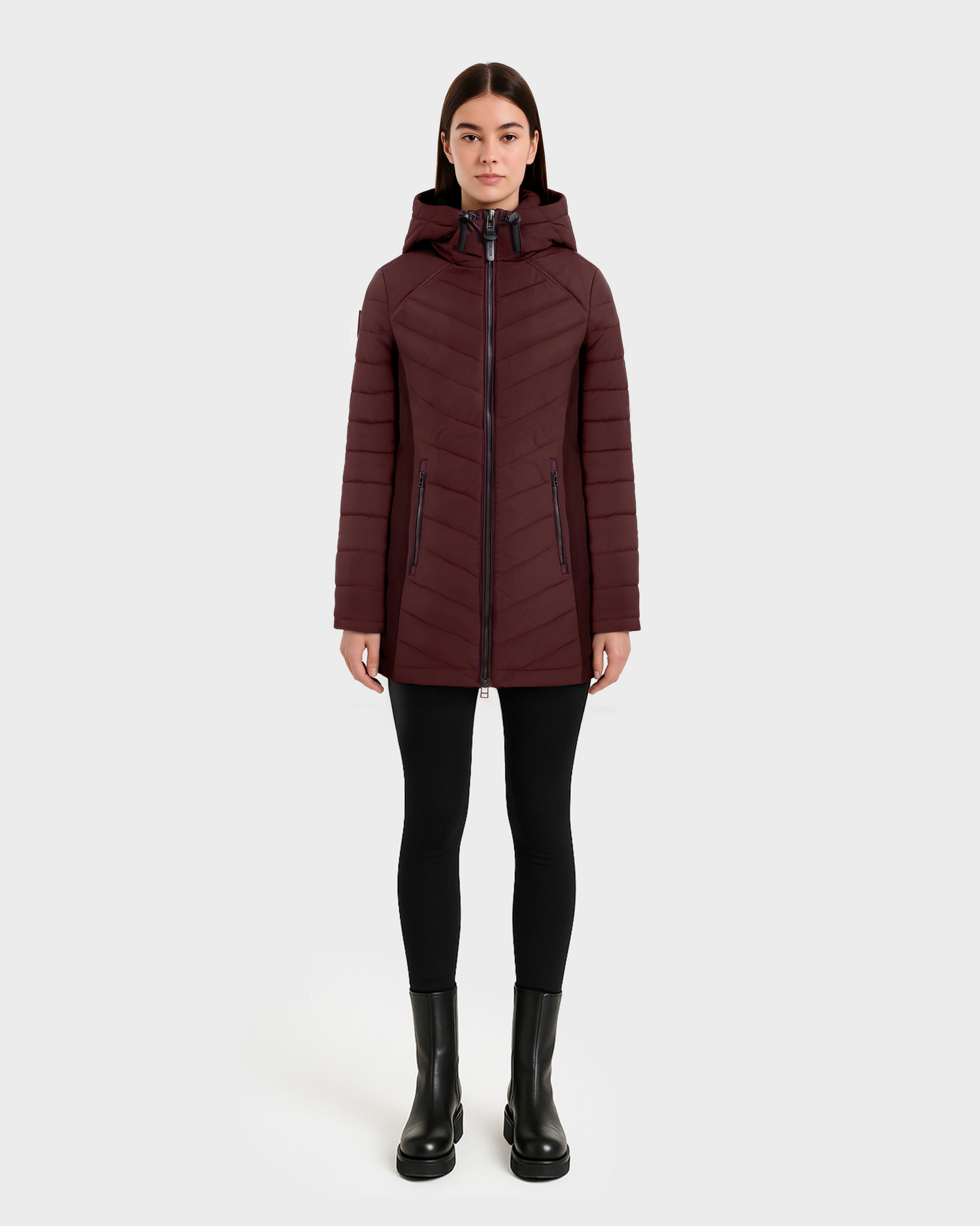 A person faces forward in a Rudsak CORDELIA - 4124519 Burgundy hooded down puffer jacket, paired with black leggings and boots, set against a plain white background.