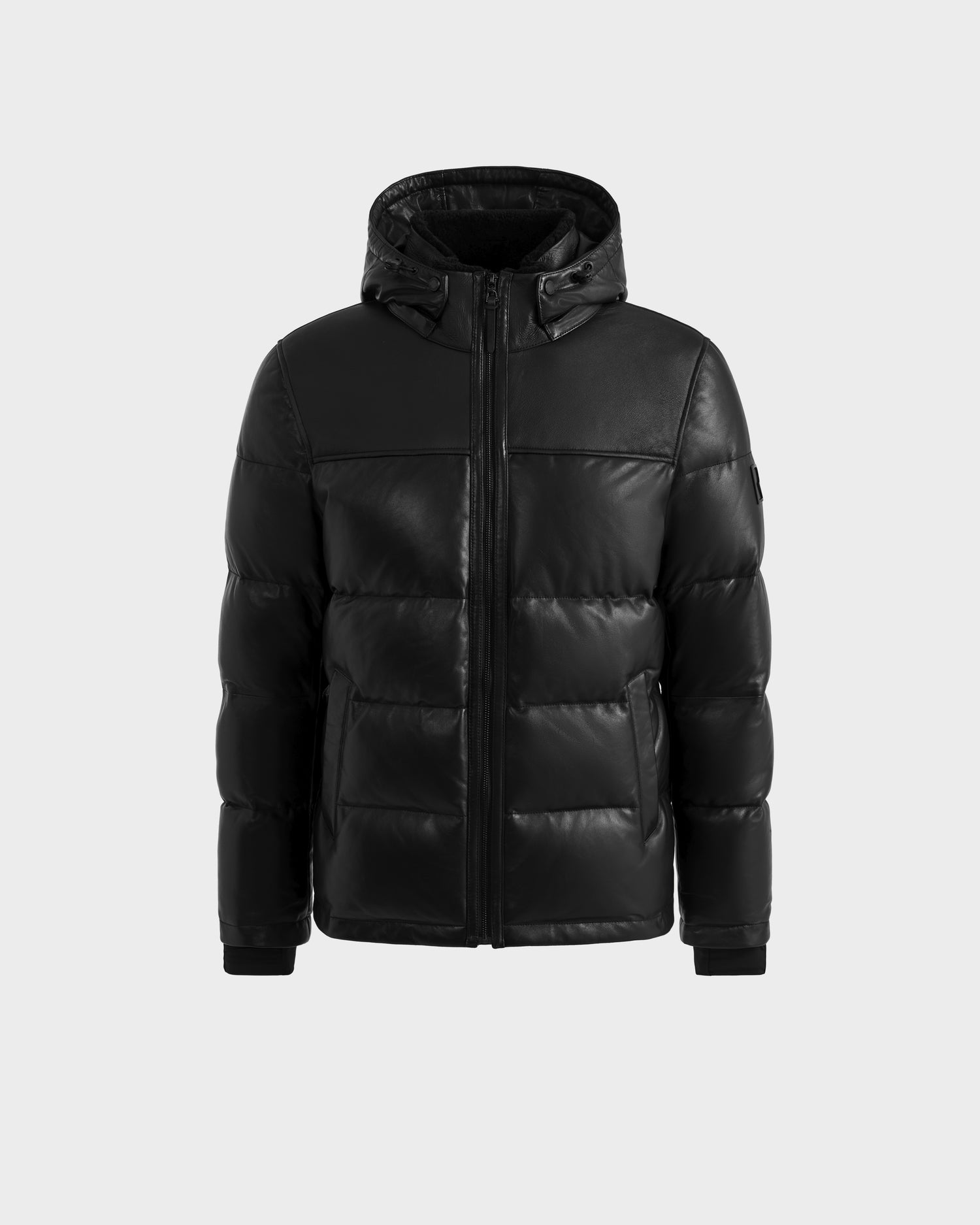 The Rudsak JAMESON - 6125678 Black men’s winter puffer jacket features a hood, front zipper, and side pockets, shown against a plain light gray background.