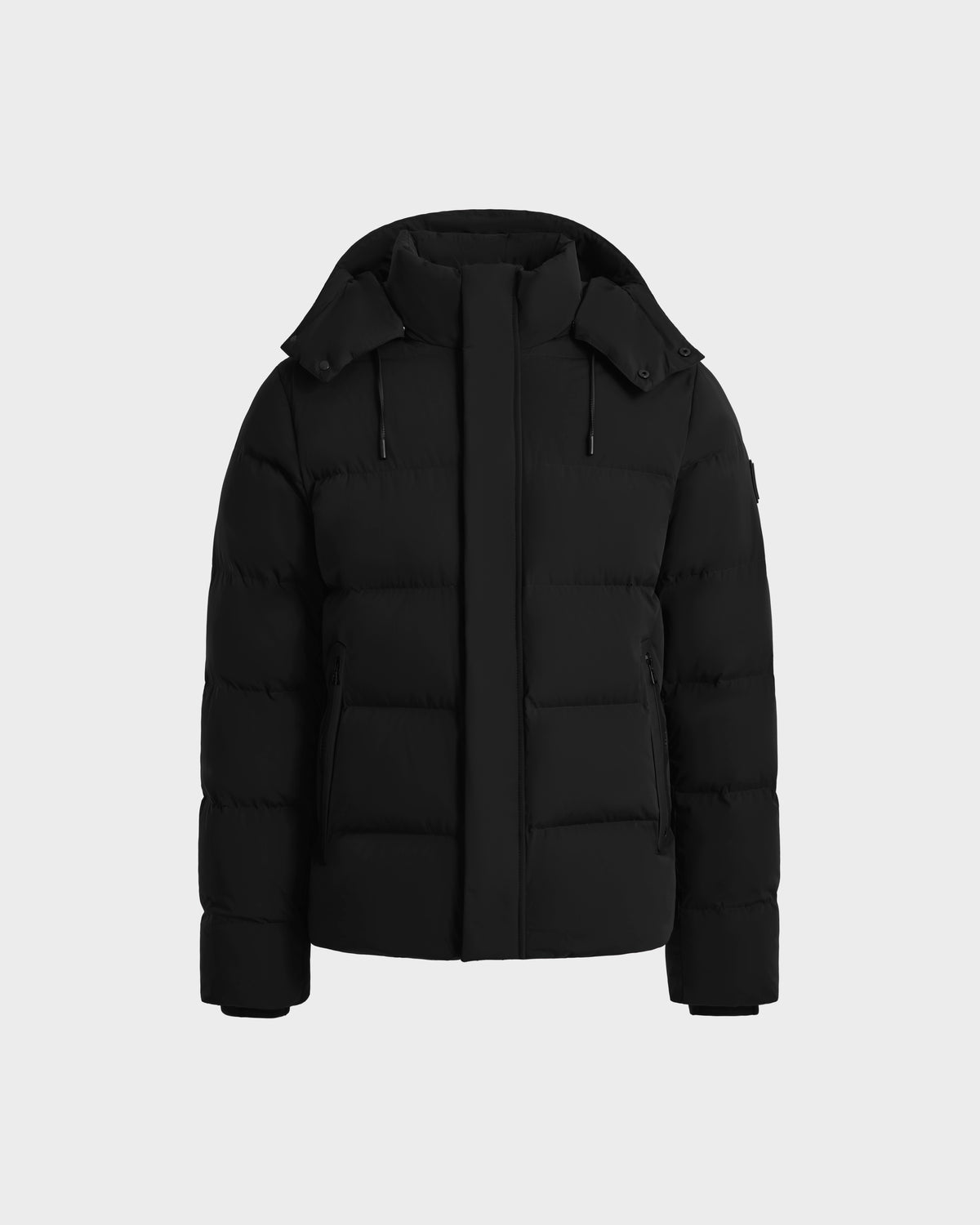 The Rudsak JOEL - 6124605 Black men’s puffer jacket, shown on a light gray background, features a high collar, detachable hood, front zipper closure, and two zippered side pockets—ideal for cold-weather wear.