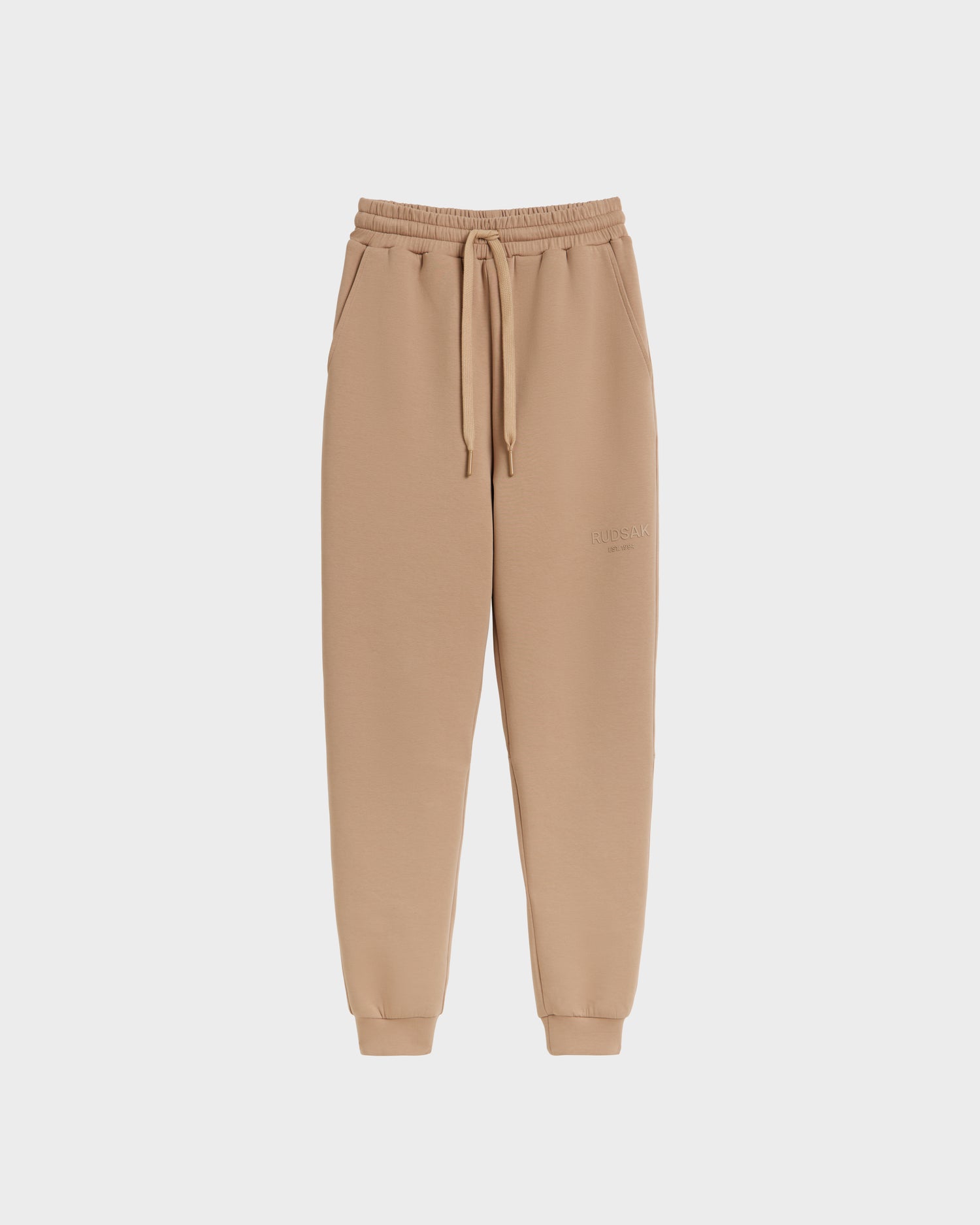 Rudsak’s JOSS - 9524009 Almond W unisex jogger sweatpants in beige, made from premium cotton with elastic waistband, drawstring, side pockets, and elastic cuffs. Shown against a plain white background.