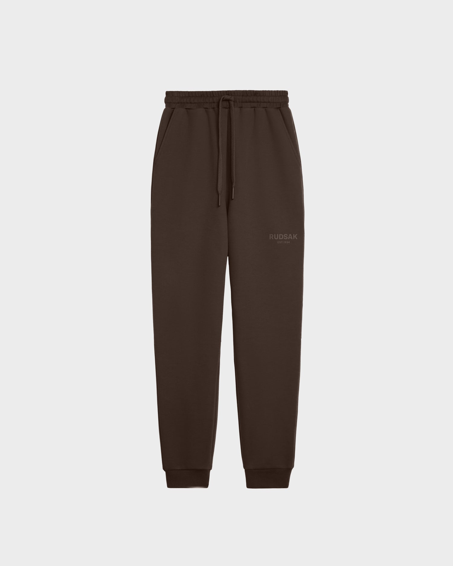 The JOSS - 9524009 Espresso M jogger sweatpants by Rudsak are made from premium cotton and feature an elastic waistband, drawstring, side pockets, cuffed ankles, a minimalist design, and a small Rudsak logo on the left thigh. Displayed on white.