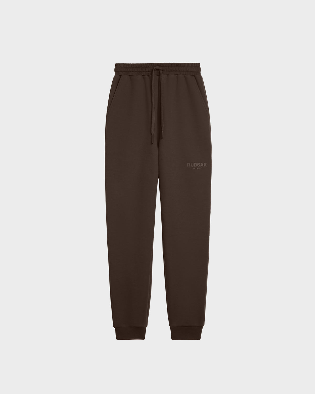 The JOSS - 9524009 Espresso M jogger sweatpants by Rudsak are made from premium cotton and feature an elastic waistband, drawstring, side pockets, cuffed ankles, a minimalist design, and a small Rudsak logo on the left thigh. Displayed on white.