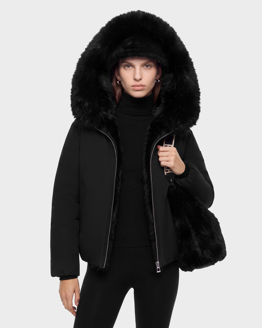 A person wears a KATHLEEN - 8126764 Black jacket with a large fur-trimmed hood and carries a black fur bag.