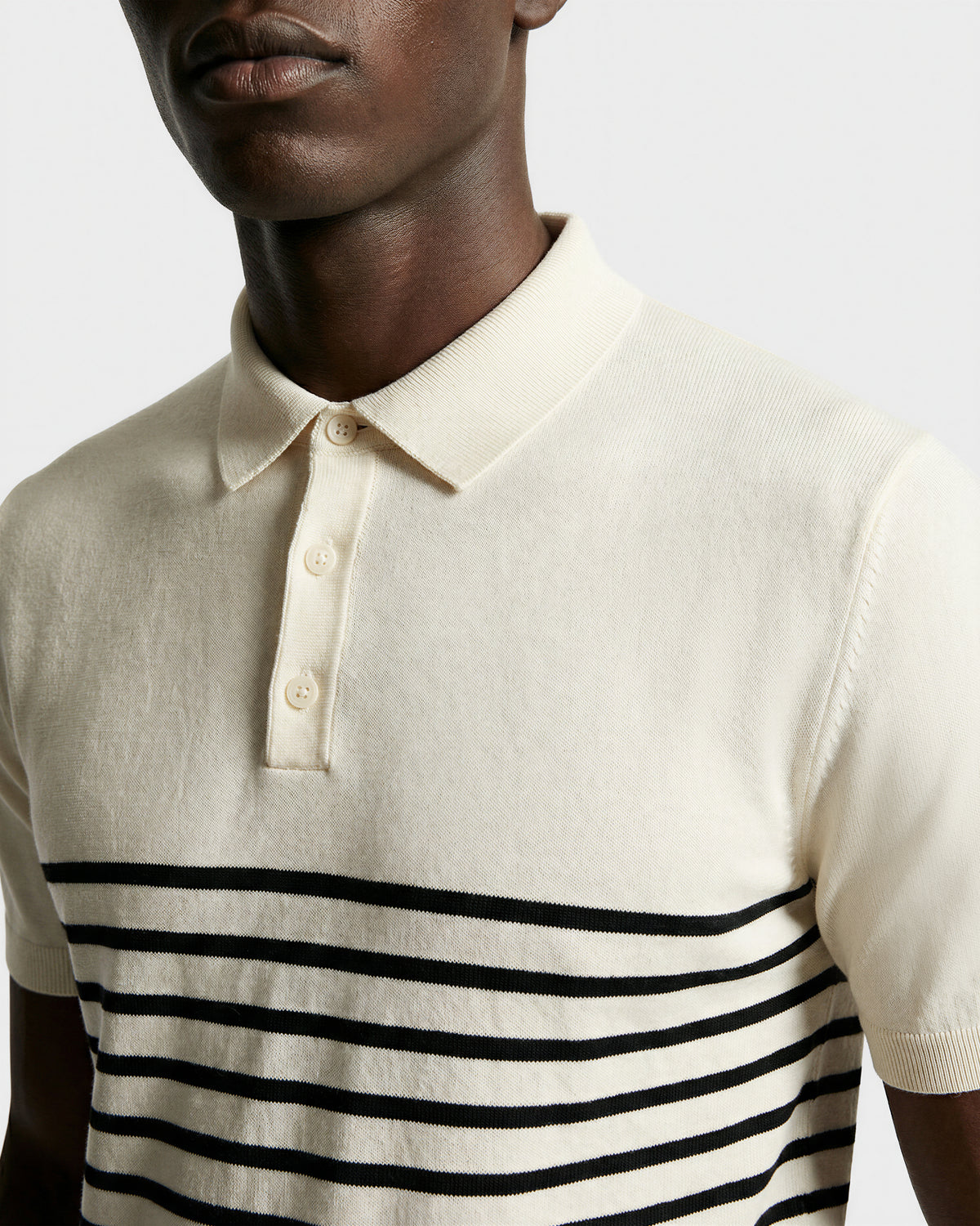 A person wearing the KRIS - 6526005 Iceland cream men's polo shirt by Rudsak, featuring a collar and black stripes across the lower chest and torso, shown from the shoulders to upper chest against a plain background.