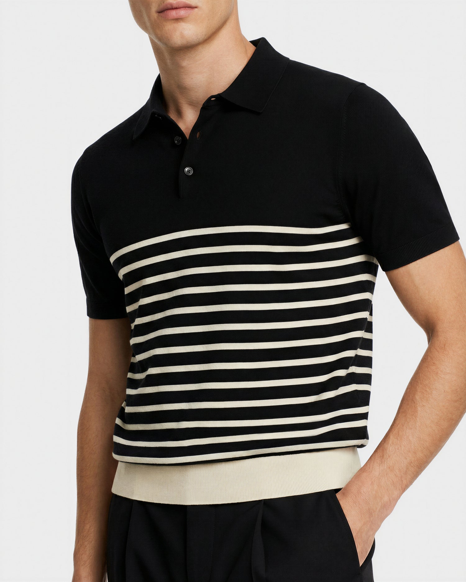 A man wears the Rudsak KRIS - 6526005 Black graphic stripe polo with a collar and horizontal white stripes, paired with black trousers. His face is partially out of frame.