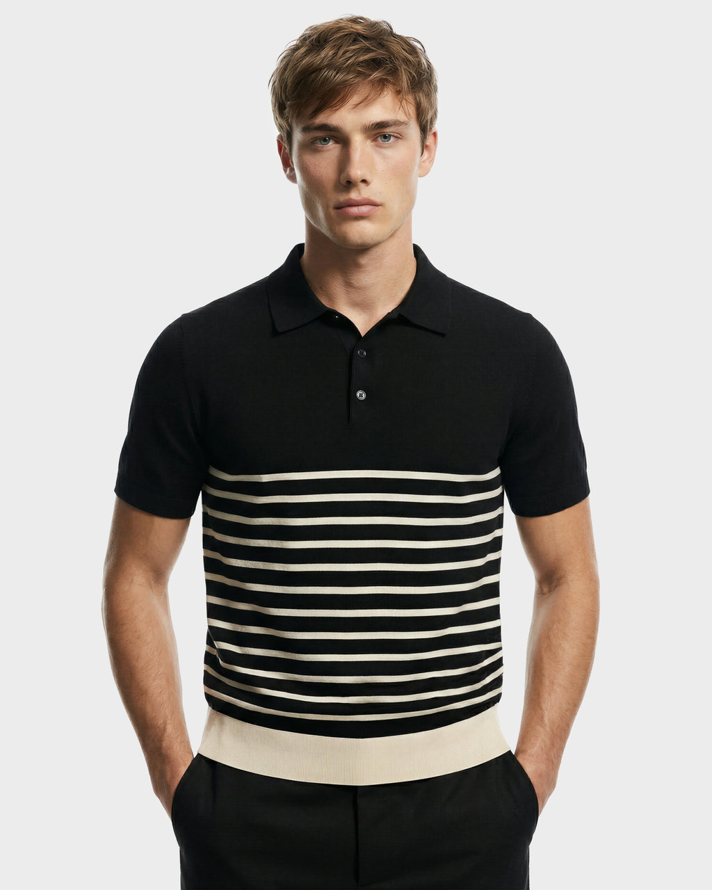 A young man wears the Rudsak KRIS - 6526005 Black contrast stripe polo, featuring horizontal white chest stripes and a solid white hem band, standing with his hands in his pockets against a plain background.