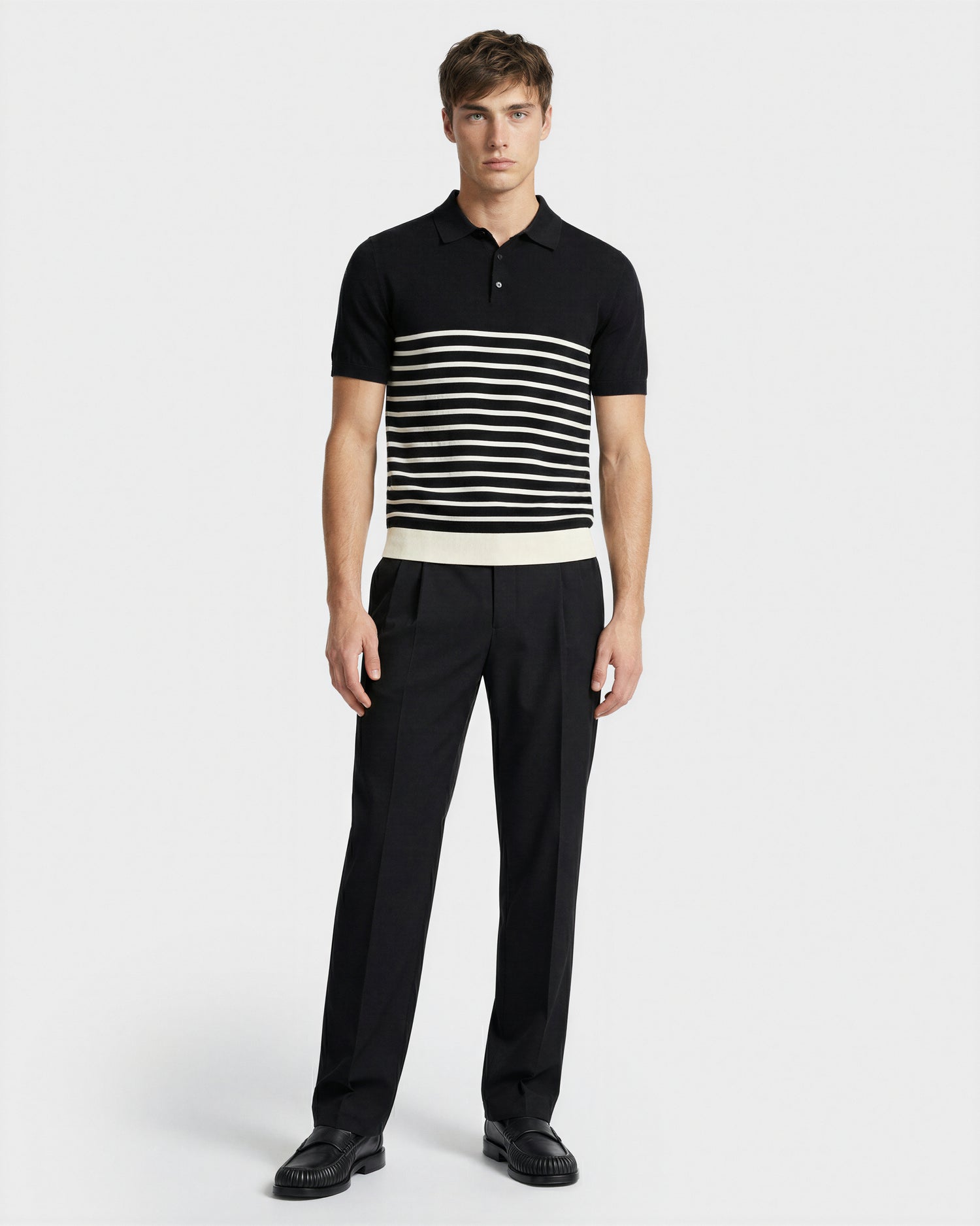 A man stands against a plain background wearing the Rudsak KRIS - 6526005 Black fine-gauge knit polo with contrast stripes, paired with black pants and shoes. He faces forward, showcasing the graphic edge of his outfit.