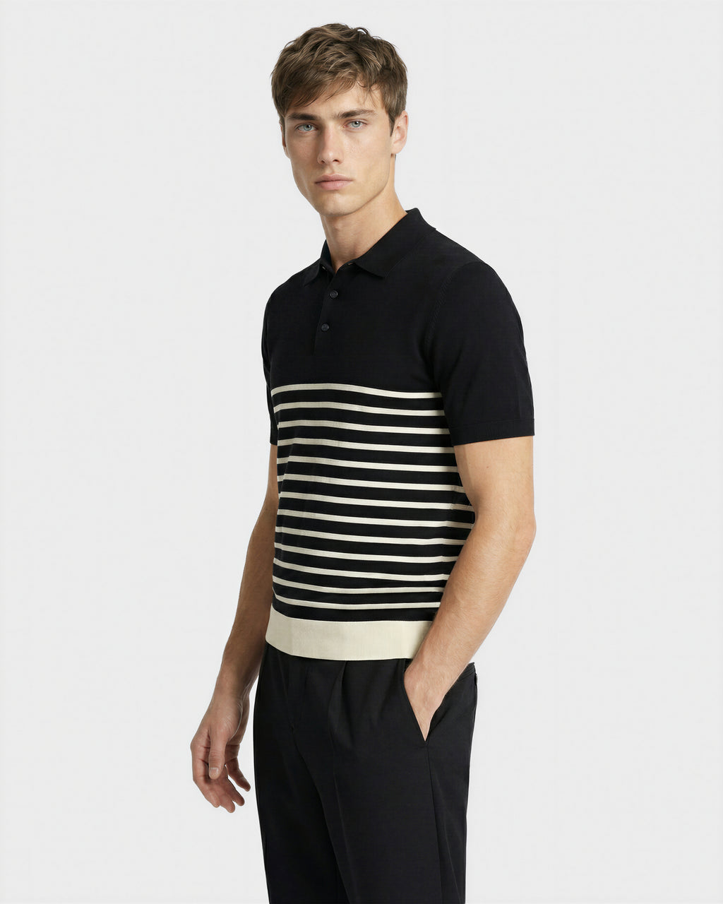 A young man wears the Rudsak KRIS - 6526005 Black fine-gauge knit polo with bold contrast chest stripes and a white hem band, paired with black pants, against a plain light background for a graphic edge.