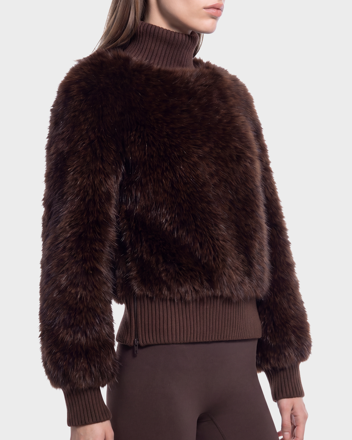 A woman wears the LAYLA F - 8525630 Mix Expresso sweater by Rudsak with ribbed cuffs, hem, and turtleneck, paired with brown pants against a plain light background.