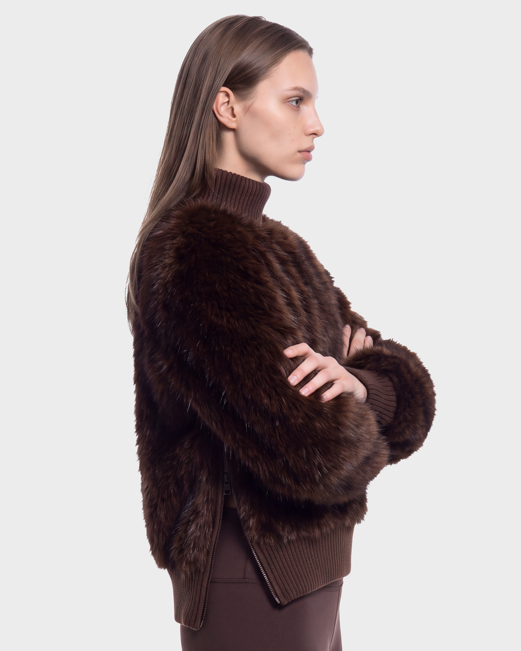 Profile view of a person wearing a Rudsak LAYLA F - 8525630 Mix Expresso dark brown faux fur turtleneck jacket with a high ribbed knit collar and side zipper details, capturing an après-ski style.