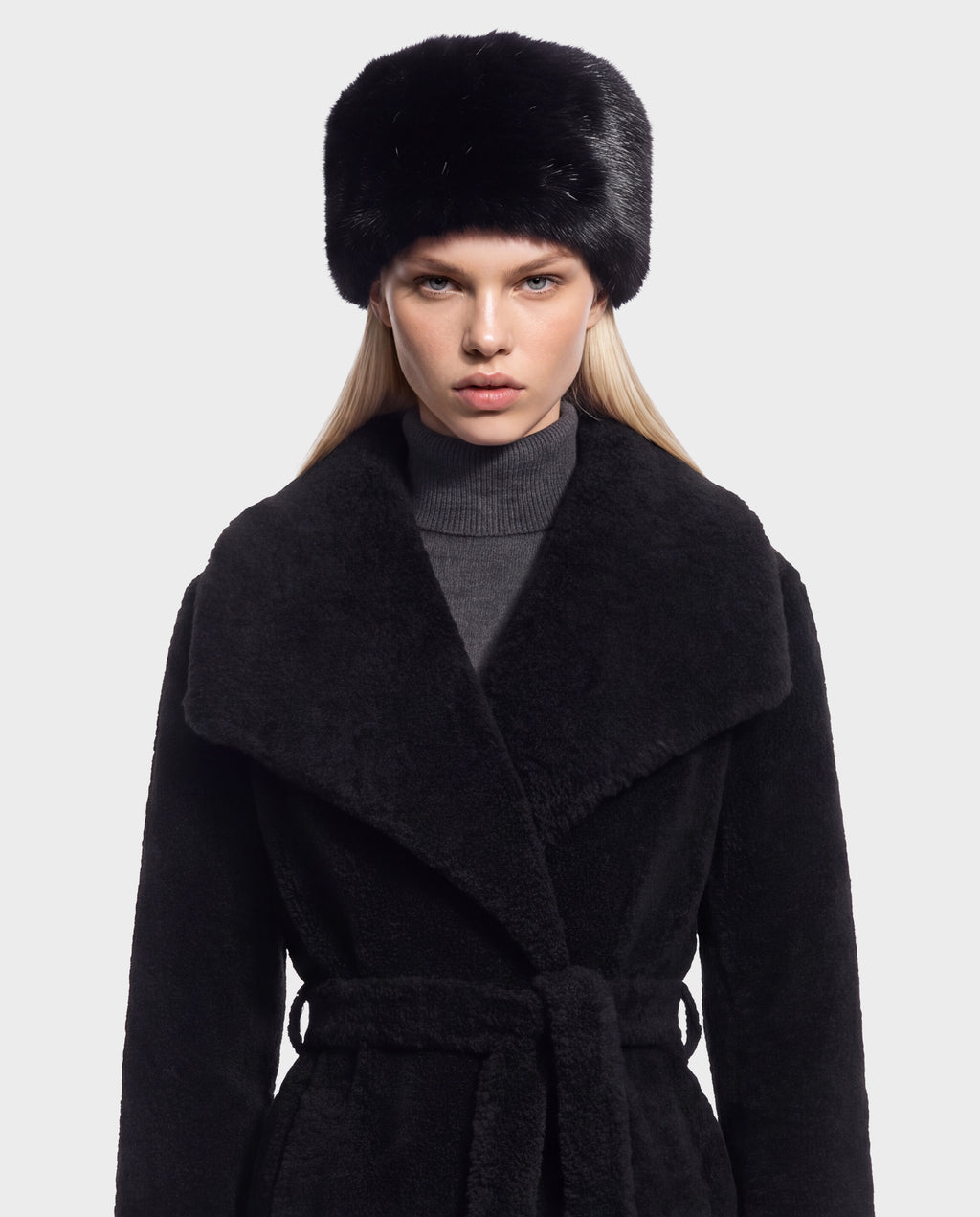 Model wearing a black faux-fur hat and a LORETTA - 8426503 Black belted coat with a wide collar over a gray turtleneck.