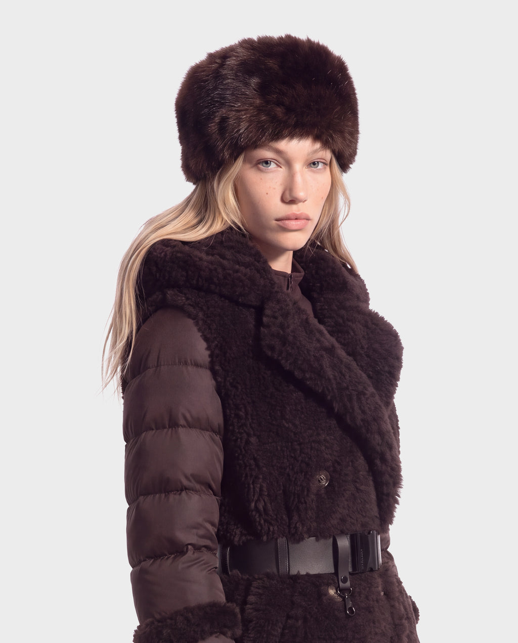A model wears a LORETTA - 8426503 Mix Espresso dark brown fur hat and a matching puffer coat with fur trim and a belted waist.