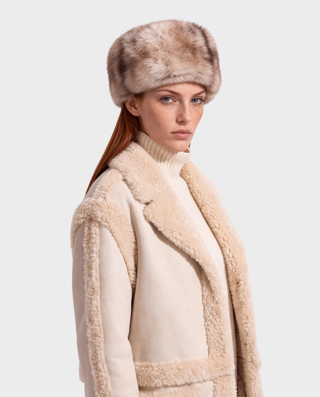 A person wearing a LORETTA - 8426503 Mix Vanilla shearling coat over a turtleneck sweater and a matching fur-style hat.