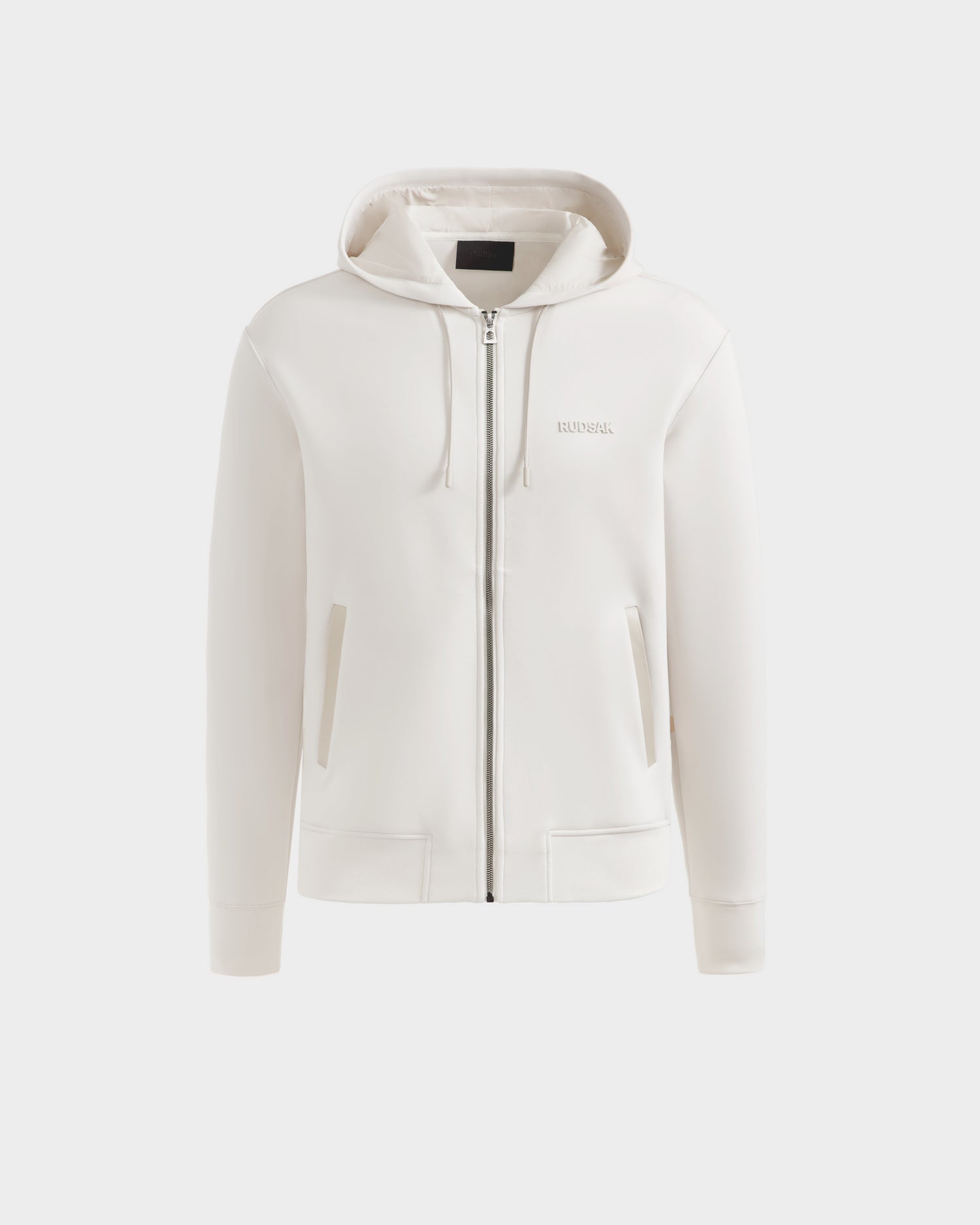 Front view of the Rudsak LEVI - 9525552 Vanilla M unisex zip-up hoodie in white, featuring subtle left chest branding, two front pockets, and a drawstring hood, shown against a light grey background.