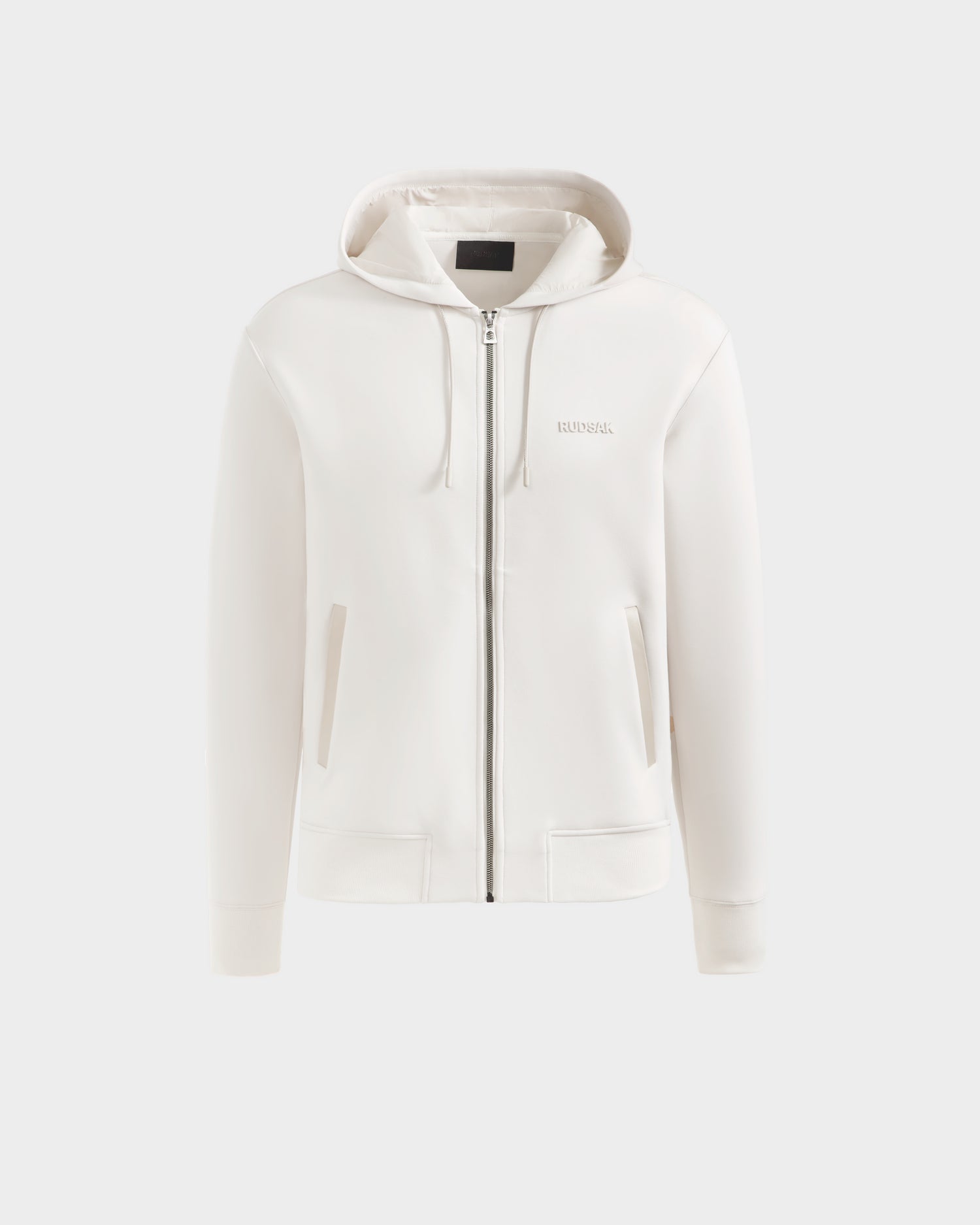 The Rudsak LEVI - 9525552 Vanilla W is a white unisex zip-up hoodie with front pockets, a hood, subtle branding on the left chest, elevated basics style, and vegan leather trims, shown against a light gray background.