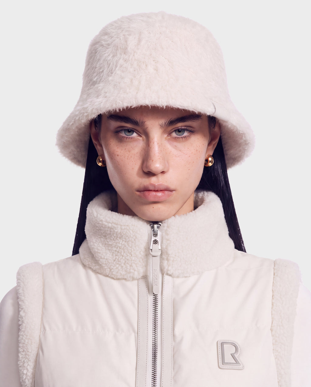 A person wearing a fuzzy cream-colored bucket hat and a matching high-neck zip-up MAIE - 8426517 Vanilla vest.