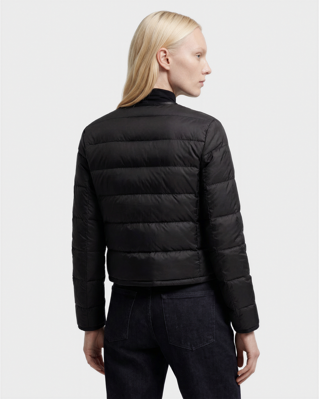 A person with long blond hair, seen from the back, wears the MARKLE - 8125033 Black women’s cropped down jacket by Rudsak with vegan leather trim and dark jeans against a plain light background.