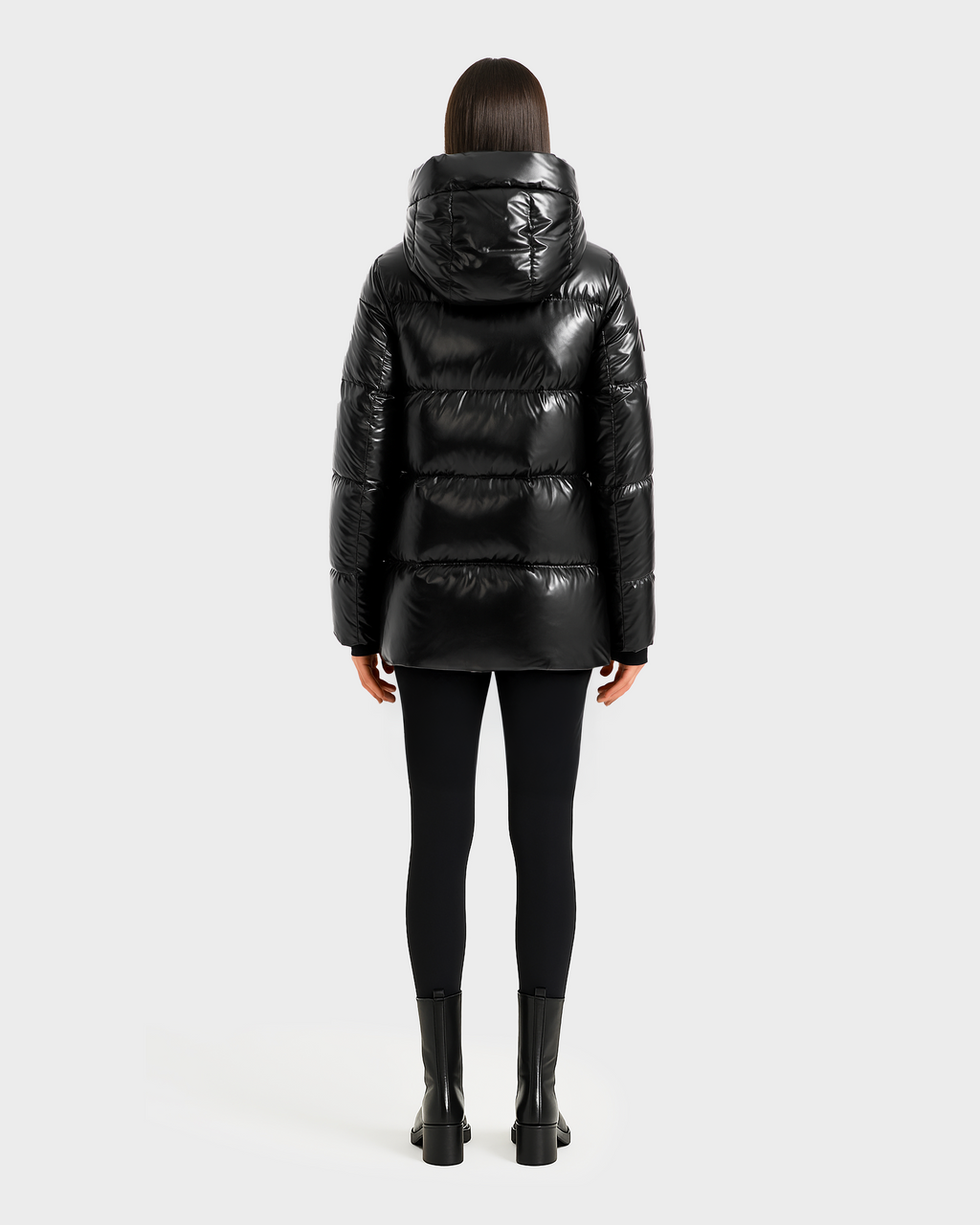 A person with straight, shoulder-length dark hair faces away, wearing the Rudsak MARY - 4124500 Black water-repellent duck down puffer jacket with black leggings and ankle boots against a plain light background.