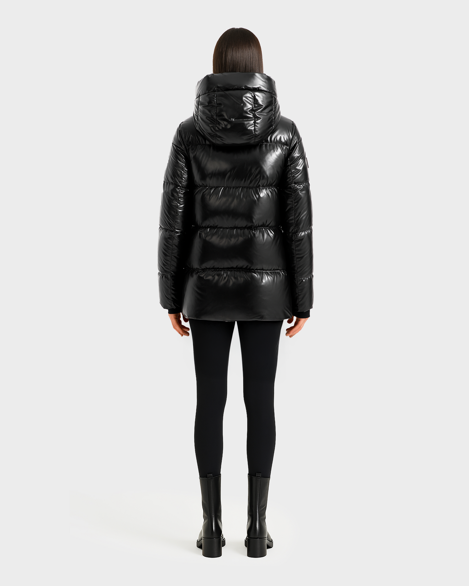 A person with straight, shoulder-length dark hair faces away, wearing the Rudsak MARY - 4124500 Black water-repellent duck down puffer jacket with black leggings and ankle boots against a plain light background.