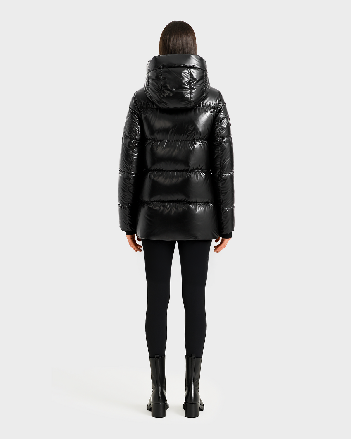 A person with straight, shoulder-length dark hair faces away, wearing the Rudsak MARY - 4124500 Black water-repellent duck down puffer jacket with black leggings and ankle boots against a plain light background.