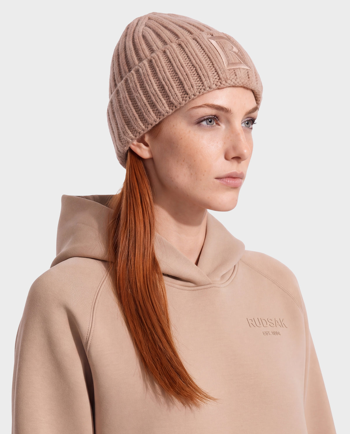 A person wearing a camel-colored ribbed knit beanie and a matching hooded sweatshirt from the Rudsak MISSA - 8426512 Camel collection.