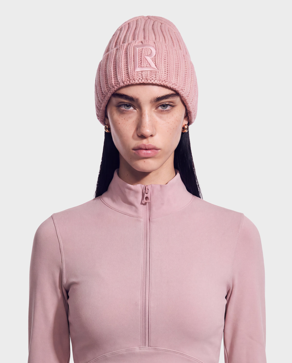 A person wearing a dusty rose MISSA - 8426512 Vintage Rose ribbed knit beanie with a centered R logo patch and a matching zip-up mock neck top.