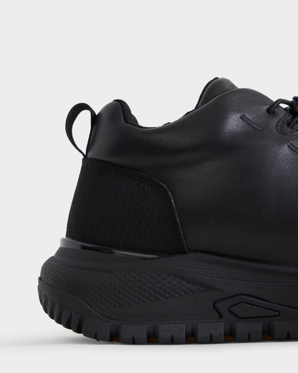Close-up of the back and side of the Rudsak MAX - 6226502 Black men’s sneaker, showcasing its textured sole, black laces, and heel pull tab. The shoe features a smooth leather upper with a ribbed fabric panel near the heel for a utility-inspired accent.