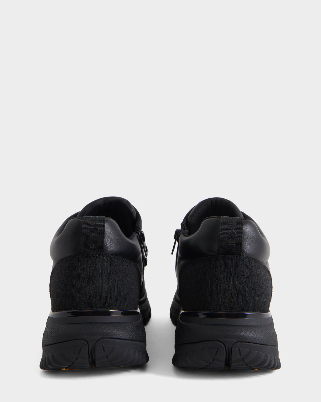 A pair of Rudsak MAX - 6226502 Black men’s sneakers is shown from the back against a plain light gray background. These utility-inspired athletic shoes feature textured soles and uppers made from a combination of smooth and knit fabrics.