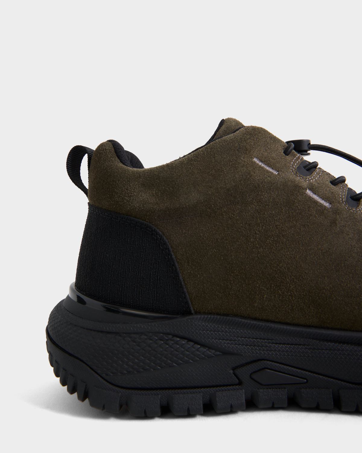 Close-up of the back half of the MAX S - 6226505 Olive men’s sneaker by Rudsak, featuring dark olive suede, a black textured rubber sole, black heel tab, and visible stitching details set against a plain light background to highlight its subtle trail-inspired design elements.
