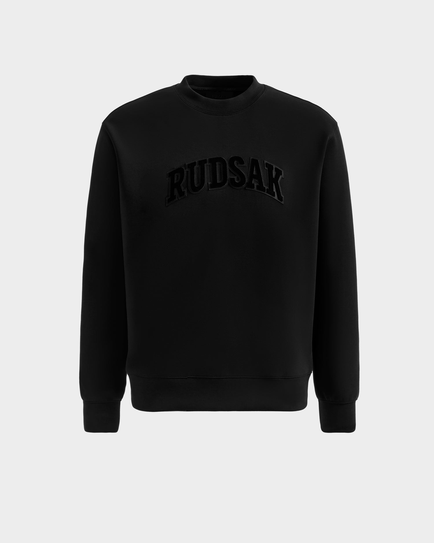 The MILOS - 6525646 Black crewneck sweatshirt by Rudsak features long sleeves and bold, textured black RUDSAK lettering on the chest. Made from a premium cotton blend, it's showcased on a plain light grey background for a modern look.