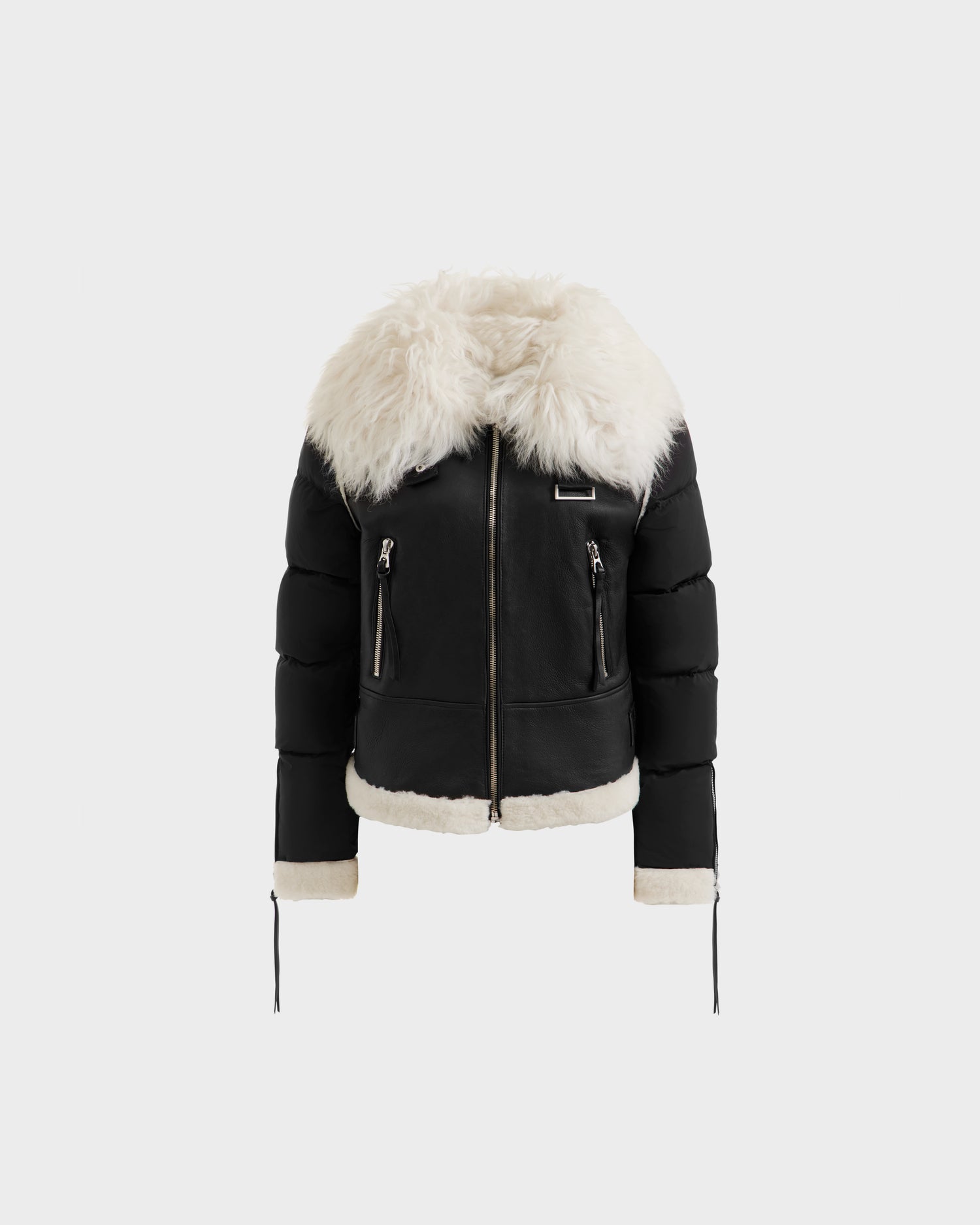 The MONKA - 8125629 Black by Rudsak is a women’s shearling jacket with a Mongolian shearling collar, silver zippers, two front zippered pockets, and plush fur lining at the cuffs and hem. Shown on a plain light gray background.