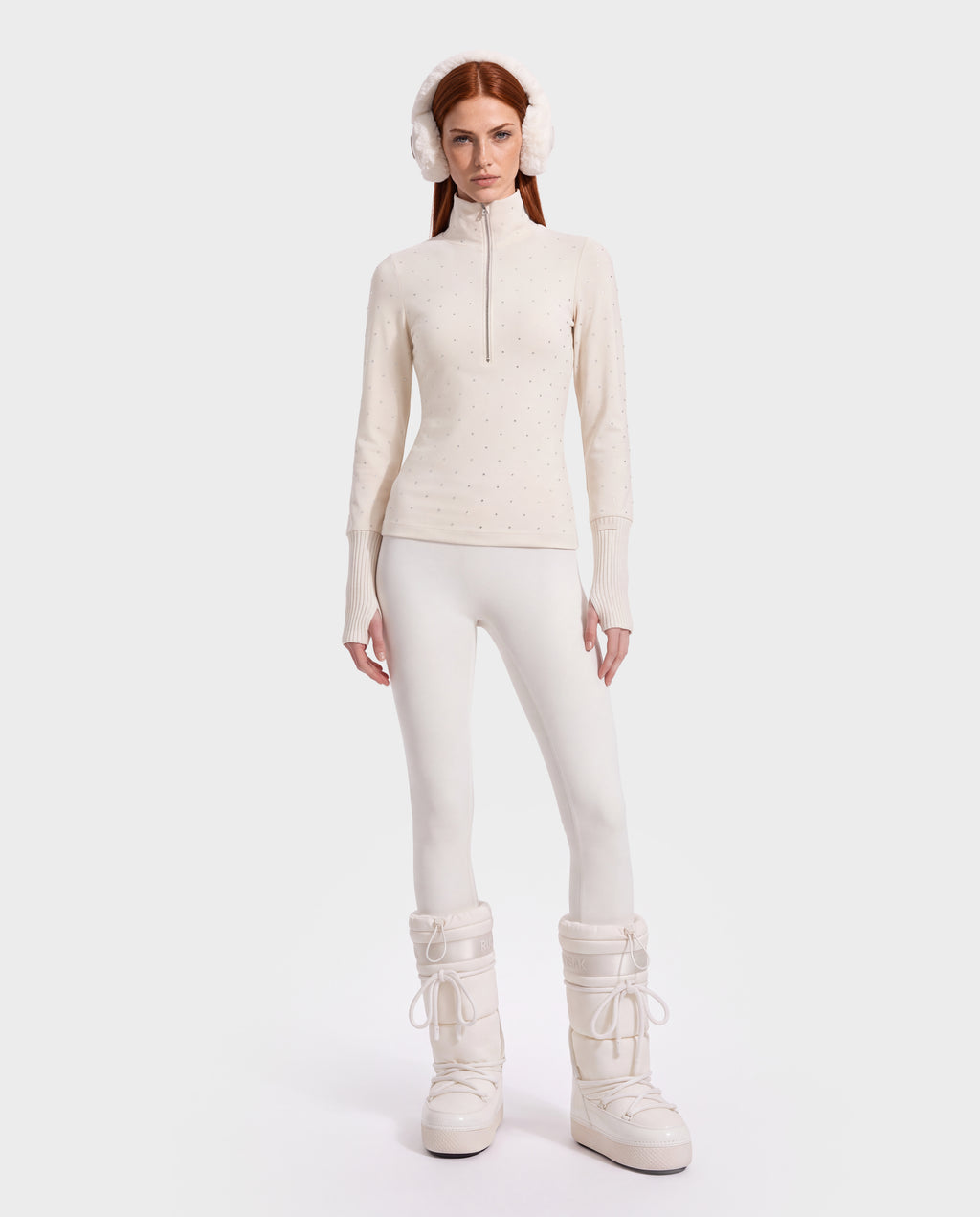 A model wears the NEVA - 8526524 Vanilla thermal long-sleeve quarter-zip top with crystal embellishments, matching leggings, white earmuffs, and tall insulated boots.