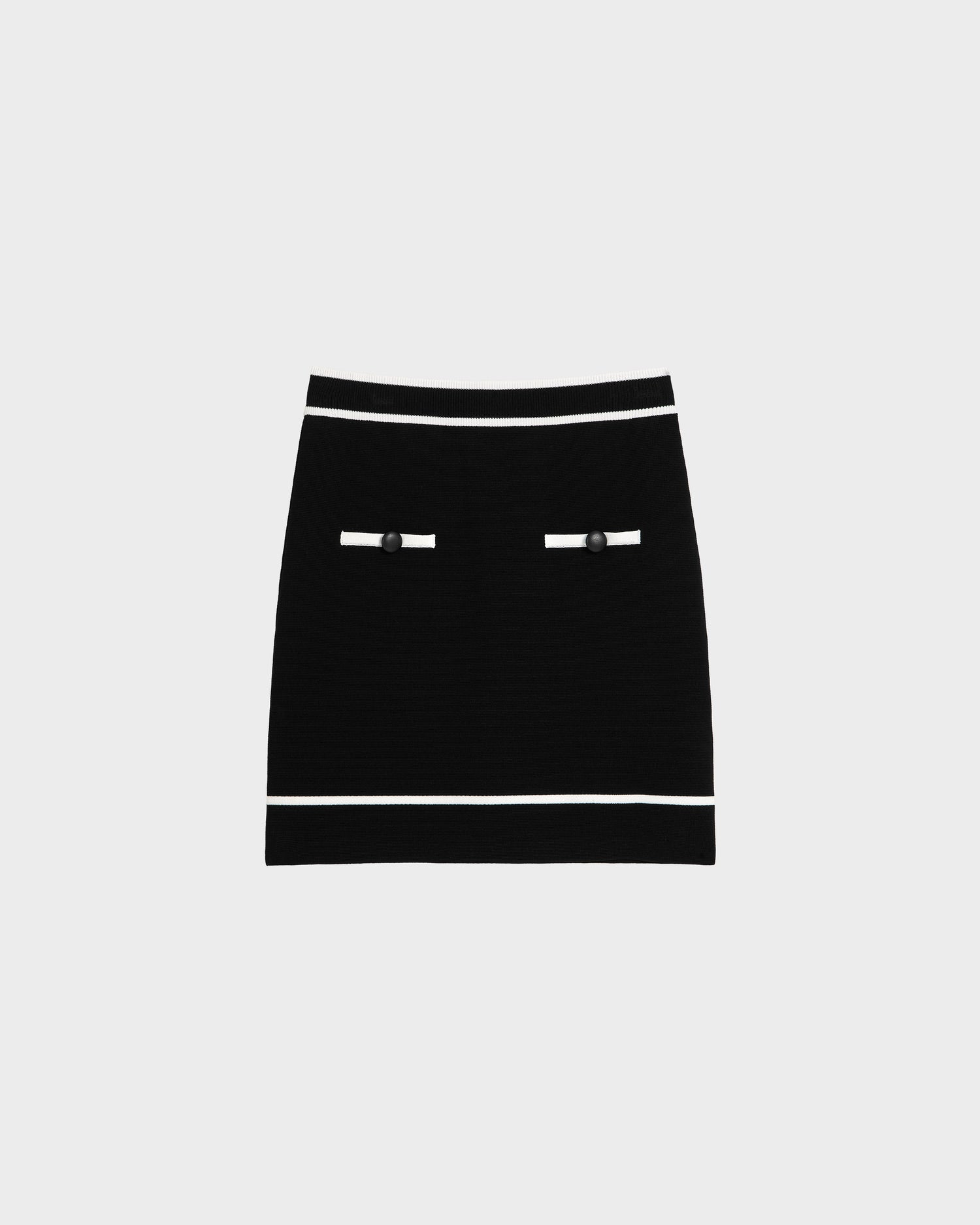 The Rudsak NAPA - 8525083 Black women’s fitted knit mini skirt features statement buttons on two white-trimmed faux pockets and contrasting trim on the waistband and hem, shown against a plain light gray background.