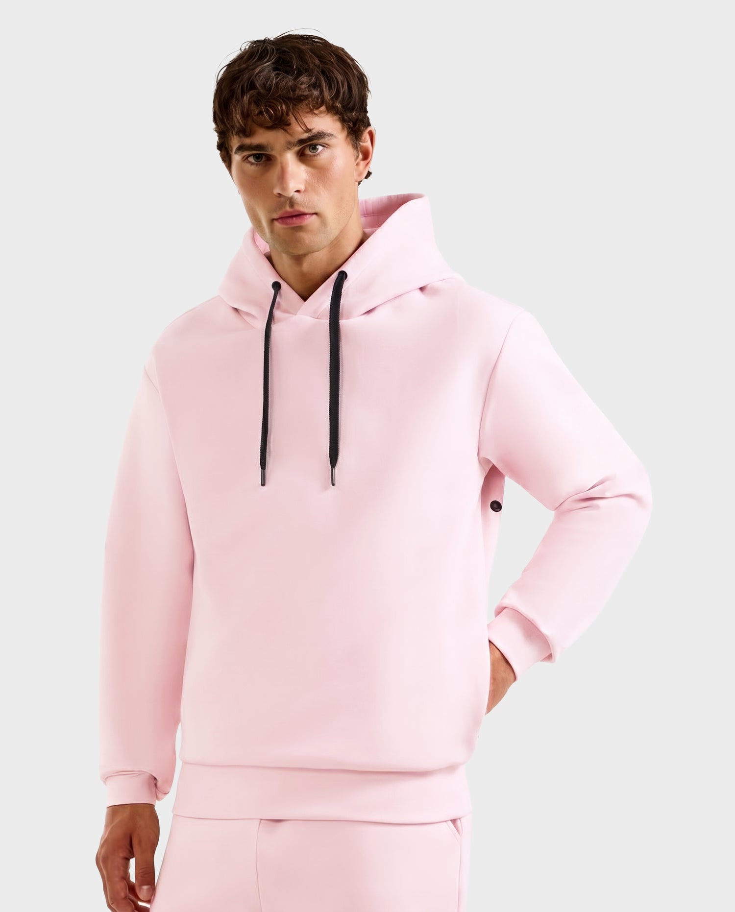 A young man wears the Rudsak LEROY - U525509 Light Pink M unisex hoodie with black drawstrings and a front pocket, posing against a plain light gray background.
