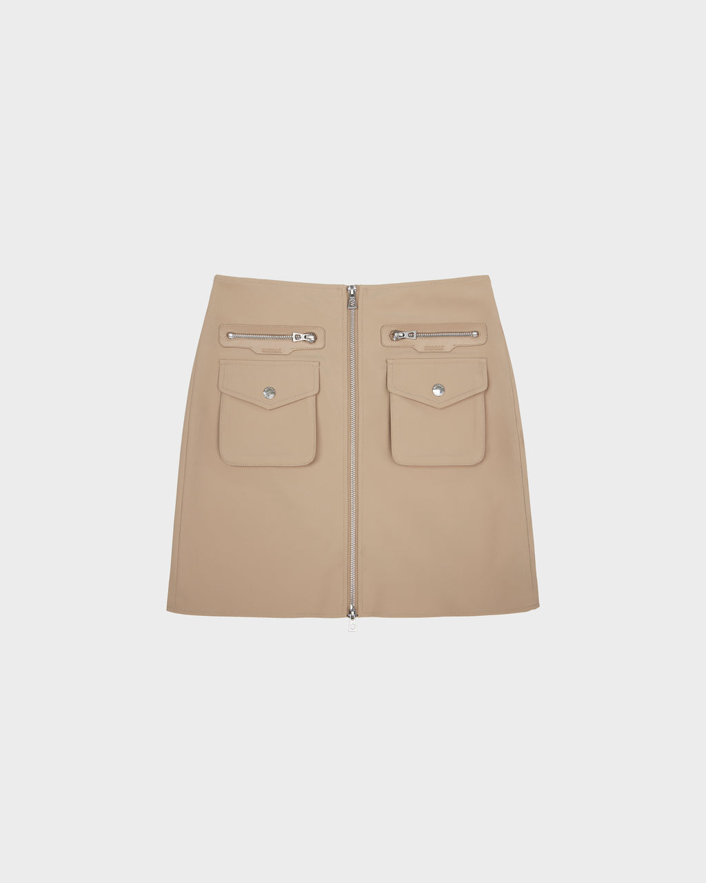 The PAMINA - 8525025 Almond mini skirt by Rudsak is made from beige vegan leather, designed with two utility flap pockets, two zippered pockets above them, and a bold front zipper. Shown against a plain white background.