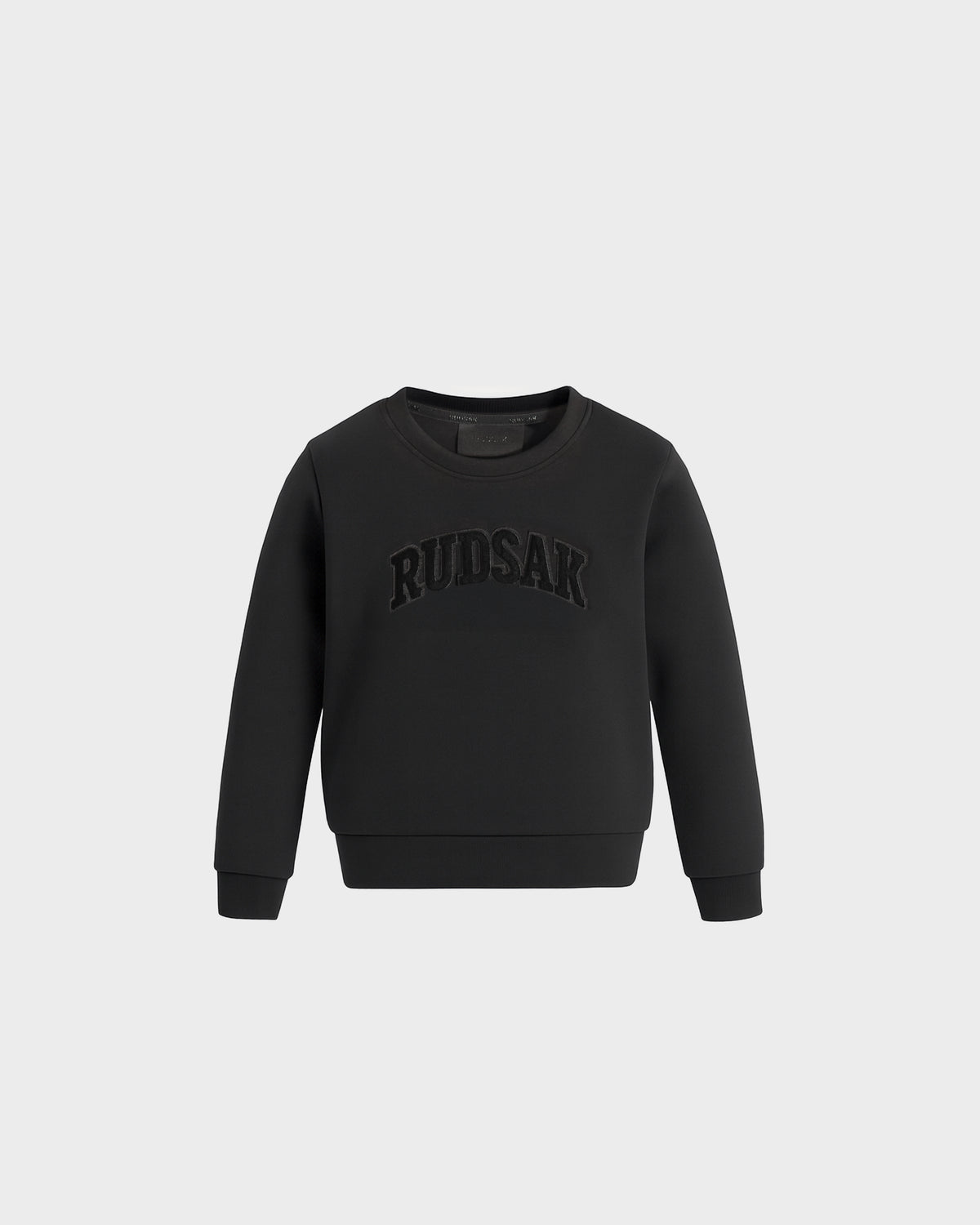 The POPPY - 1525003 Black by Rudsak is a black long-sleeve sweatshirt featuring black RUDSAK embroidery on the front, shown against a plain light gray background.