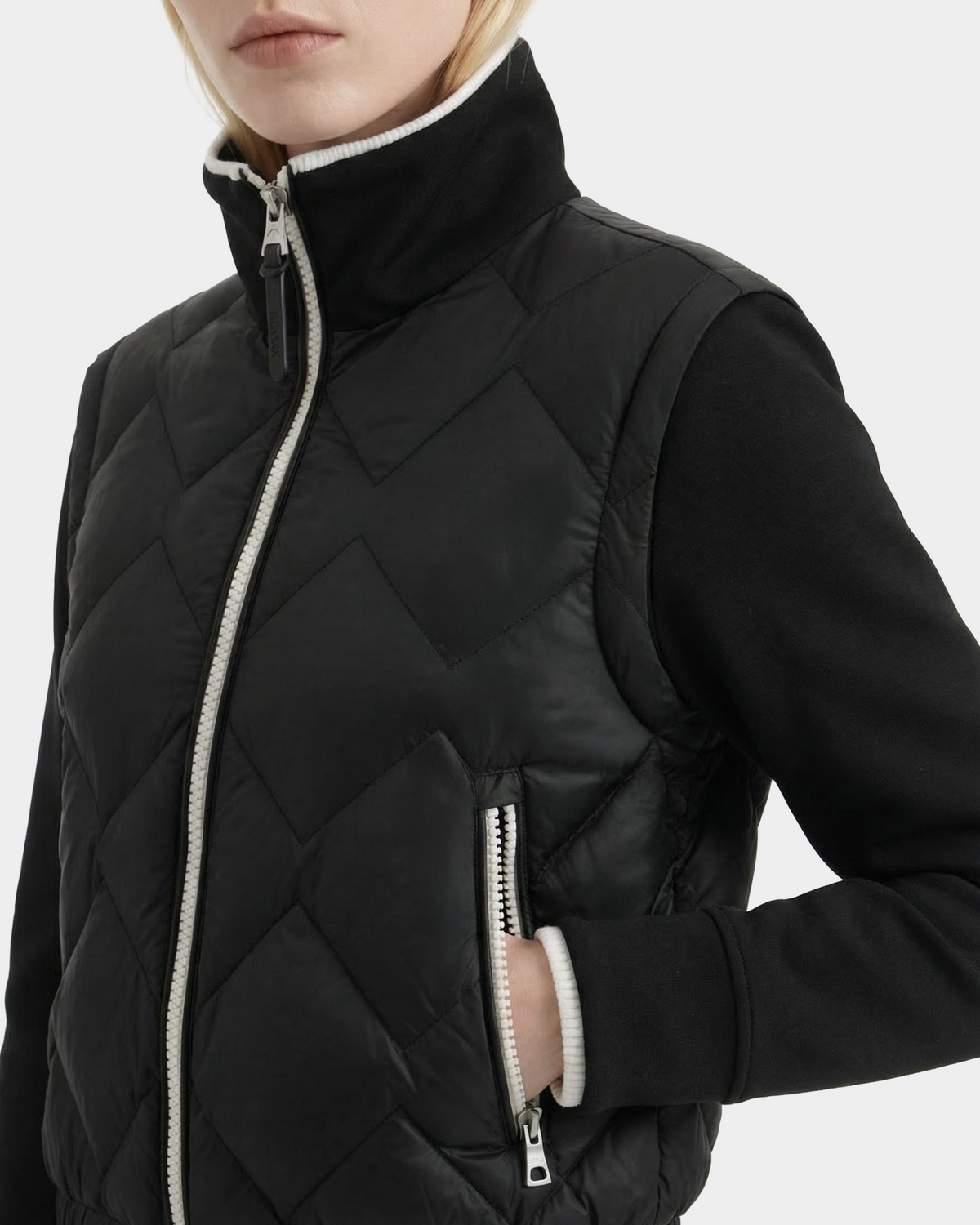 A woman wears the PRISA - 8126022 Black quilted jacket by Rudsak, featuring a high collar and white zipper, layered over a black long-sleeve top. The image is cropped at the shoulders and midsection.