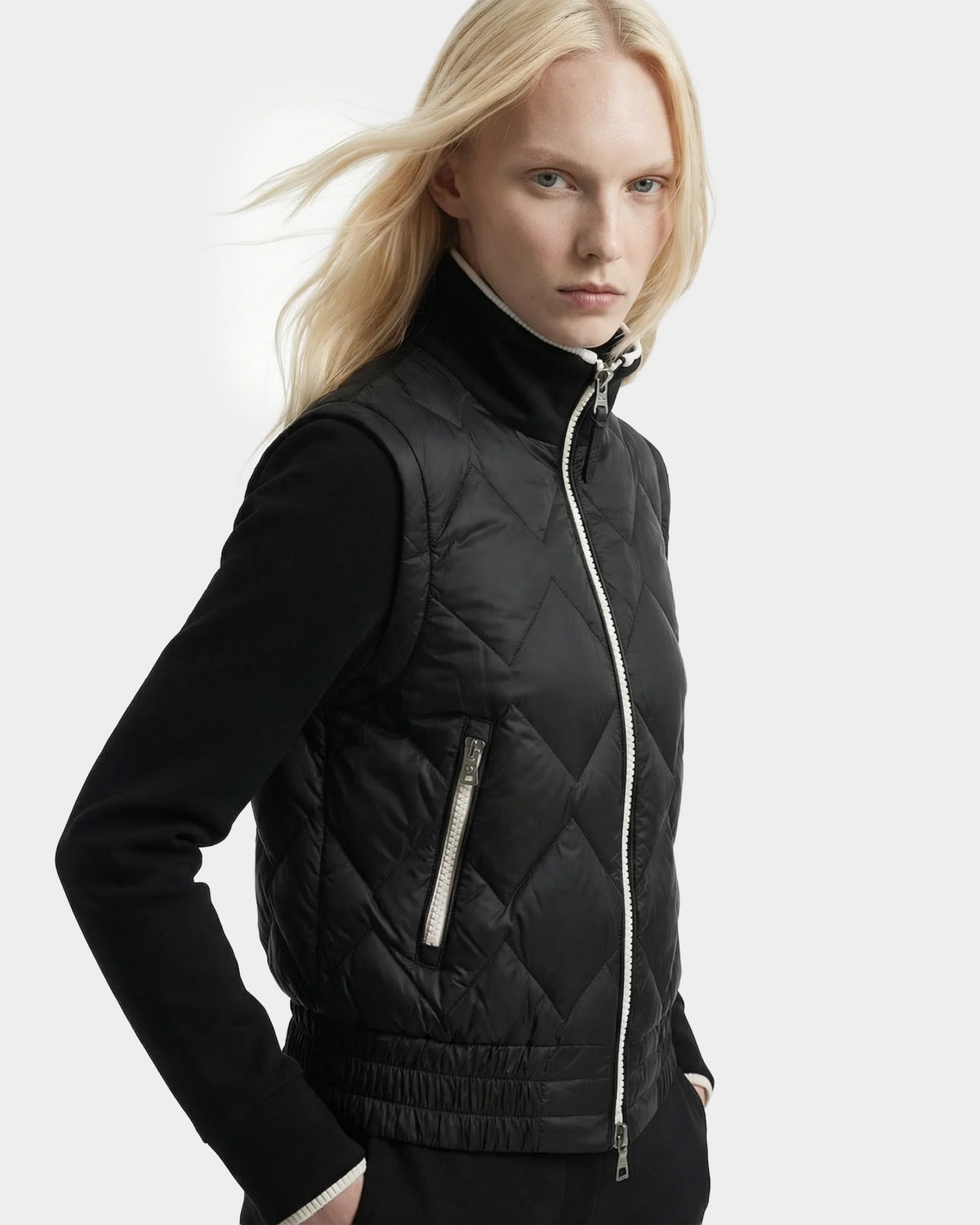 A person with long blonde hair wears the Rudsak PRISA - 8126022 Black quilted vest with removable sleeves over a black top, standing against a plain light background and looking slightly to the side.