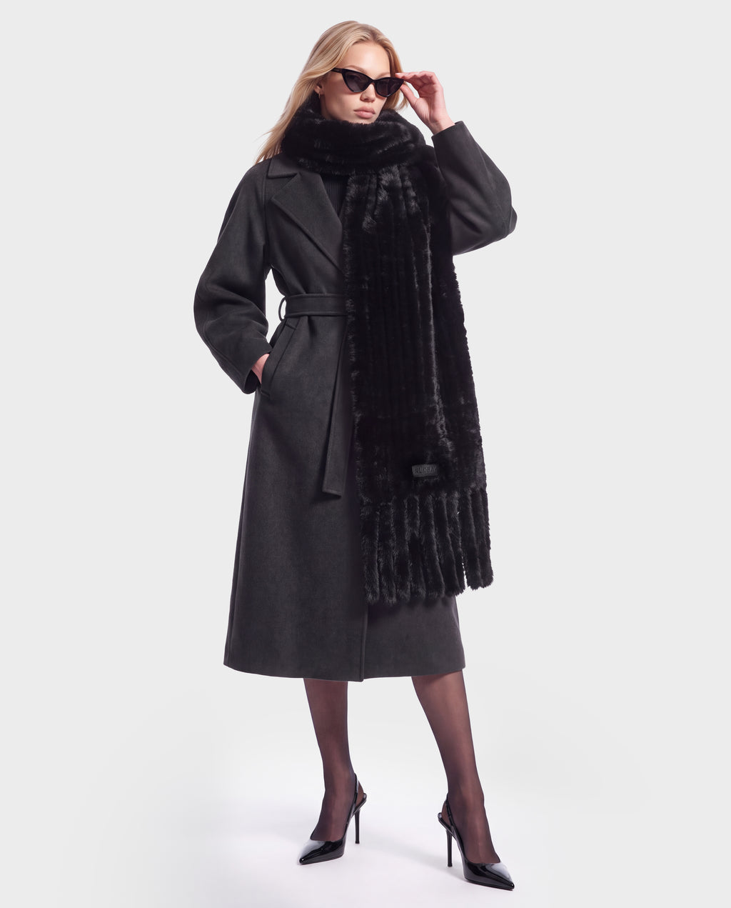 A person wearing the Rudsak TAVIA - 8426511 Black belted wool coat, a luxurious faux fur scarf, and sunglasses.
