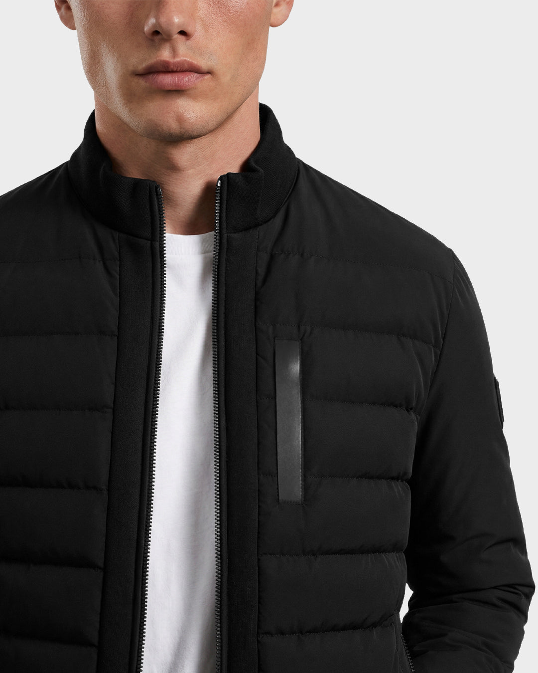 A person wearing the Rudsak JIMMY - 6125723 Black men's quilted down jacket, zipped up over a white T-shirt, shown from shoulders to upper chest with a partially visible face.