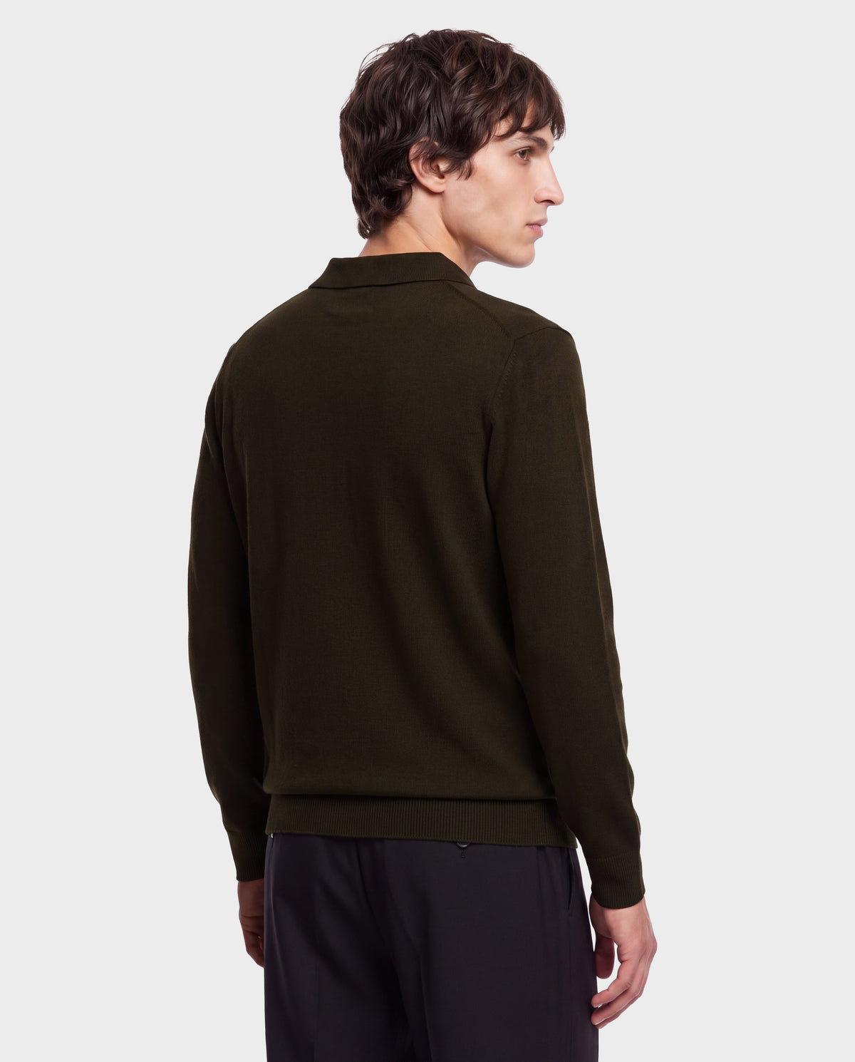 A person with short brown hair, wearing the Rudsak RICHARD - 6524529 Olive men’s knit polo sweater and black pants, stands facing away and looks over their left shoulder against a plain white background.