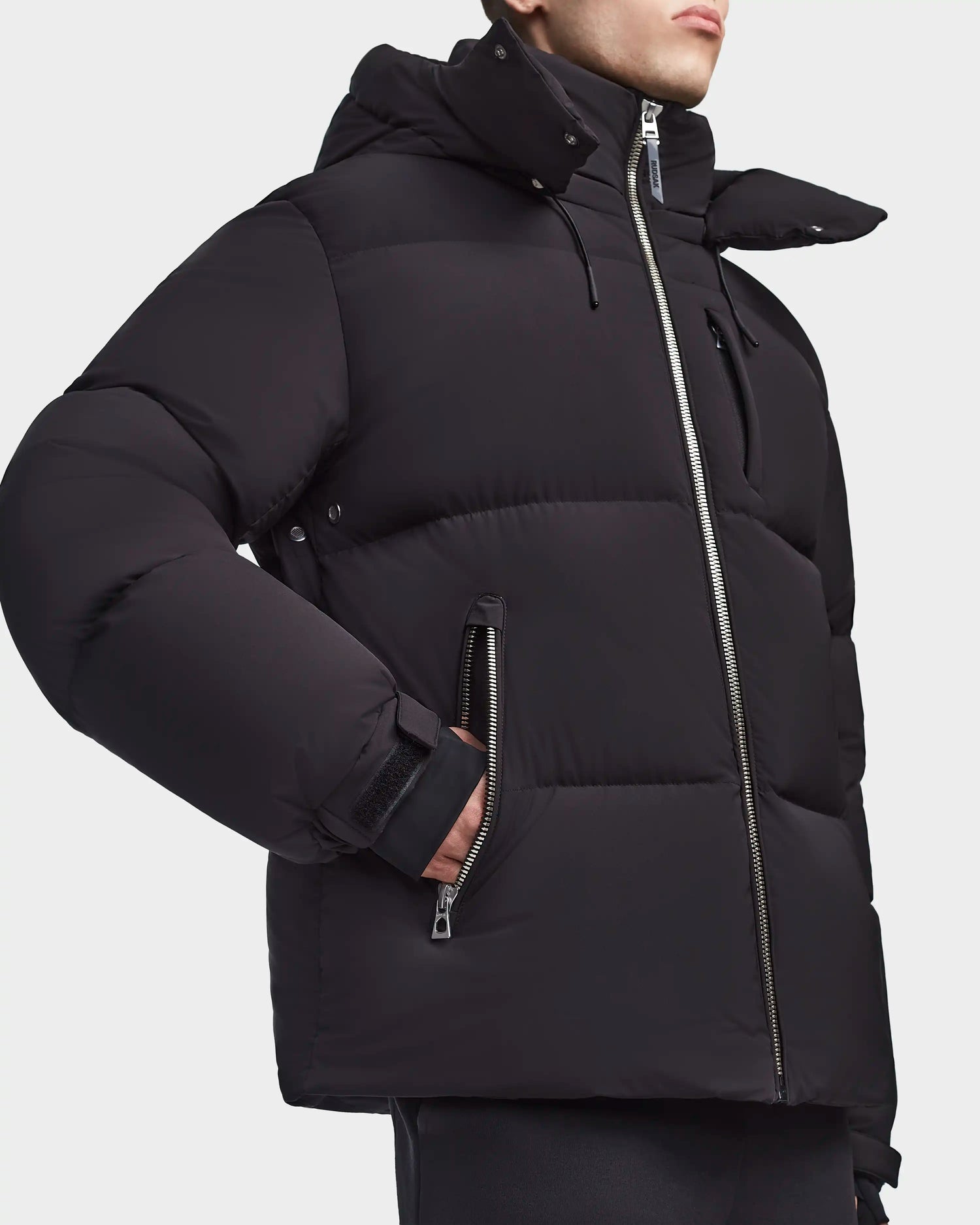 Model wearing the Rudsak VINCENT M - 6123510 Black men's down puffer with lightweight insulation and zippered pockets, shown from shoulders to hip against a plain background.