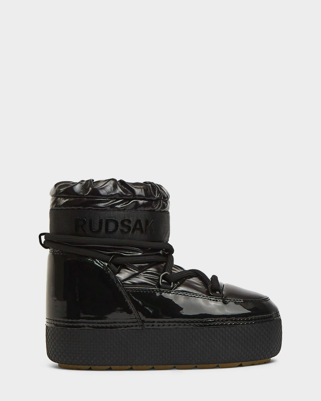 The Rudsak MACE - 8223500 Black is a women’s black short moon boot with a high-shine finish, chunky sole, thick laces, water-repellent exterior, quilted padded ankle cuff, and embossed RUDSAK branding on the cuff. Shown side view on white.